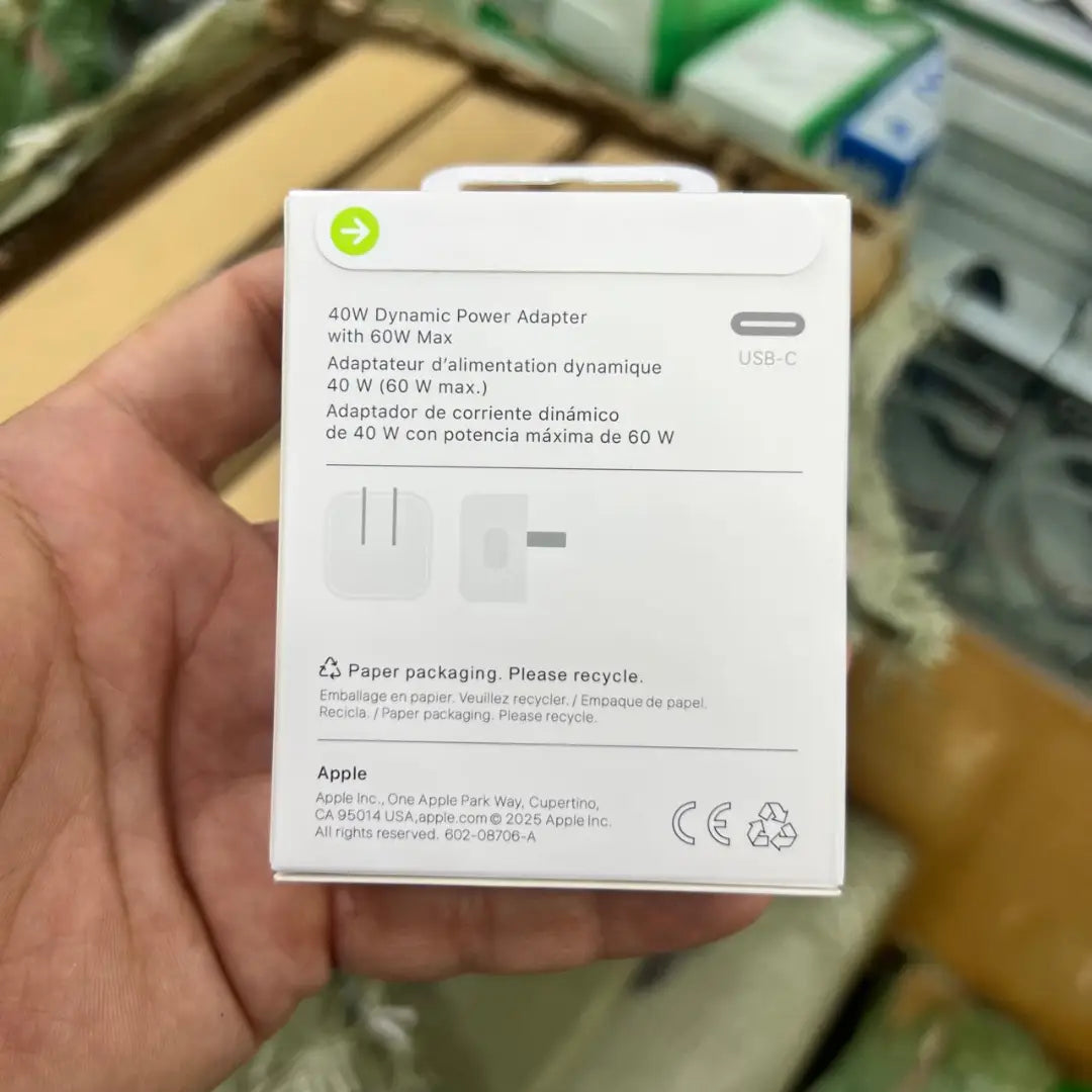 Hand holding a white power adapter box with Apple branding.